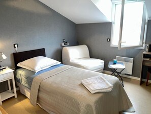 Un dormitorio con dos camas, un escritorio, una silla, un ventanal y un radiador.
