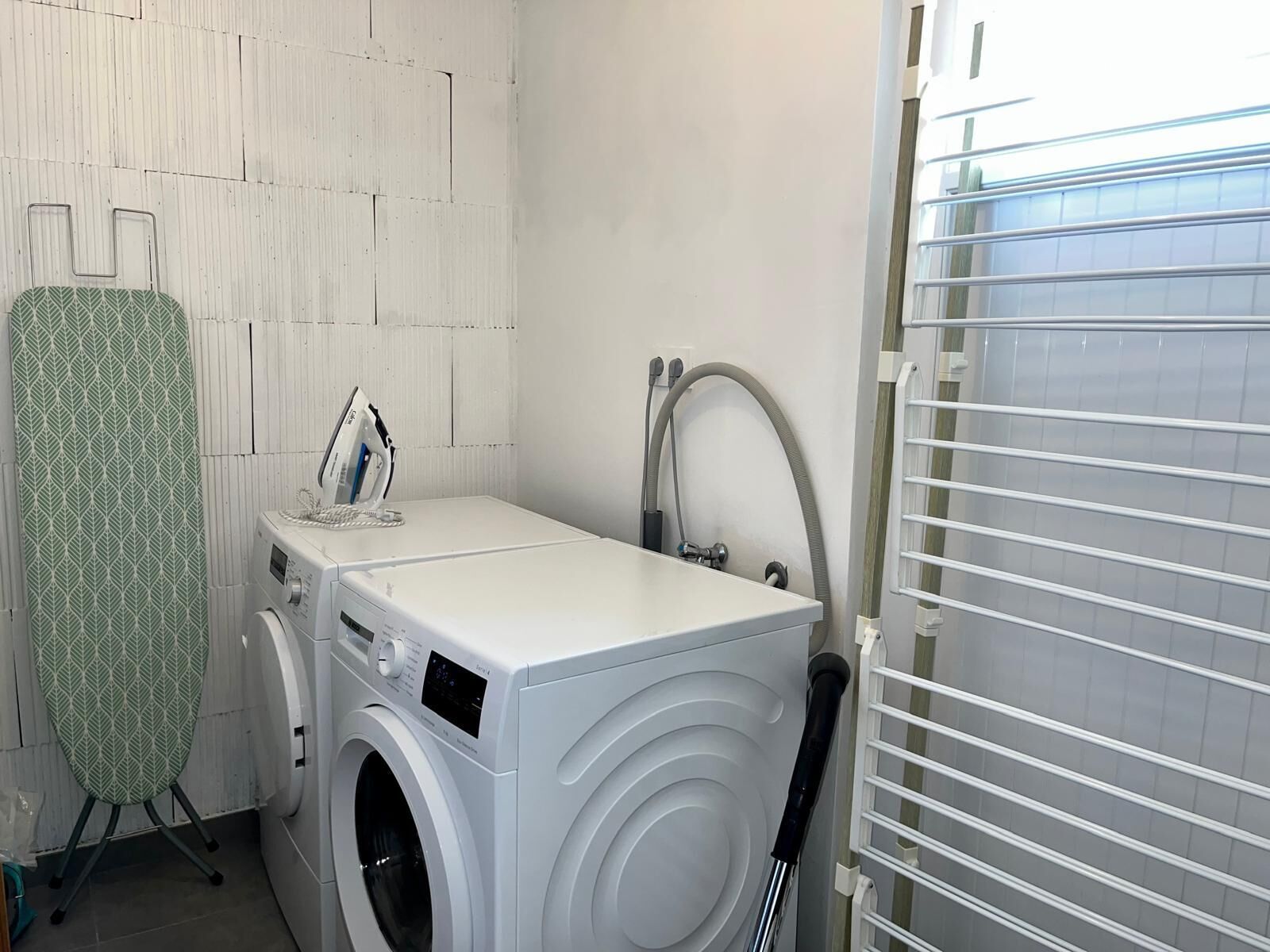 A compact laundry area with a washing machine, an iron, and a drying rack.