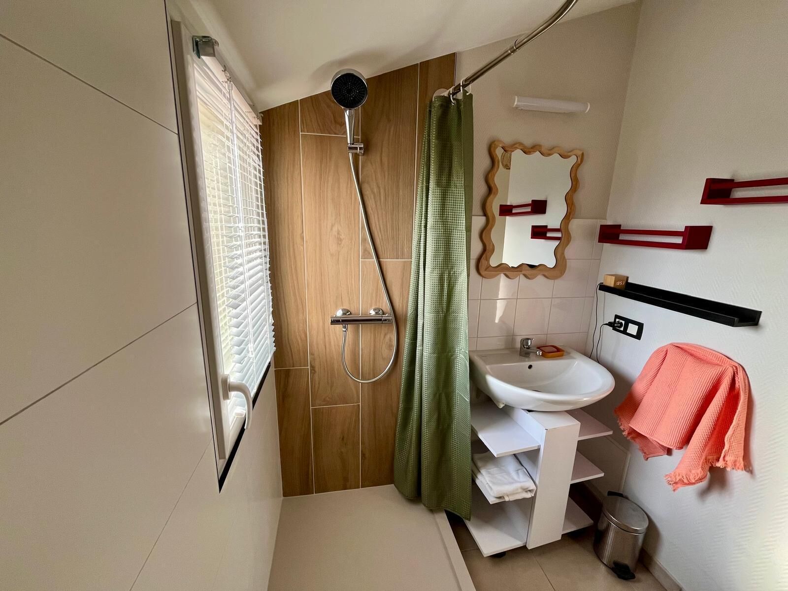 A bathroom with a shower, a sink, a mirror, and a towel rack.