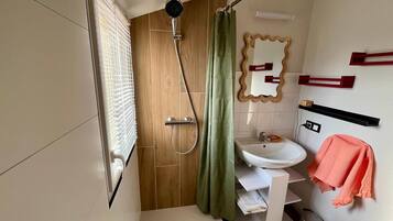 A bathroom with a shower, a sink, a mirror, and a towel rack.