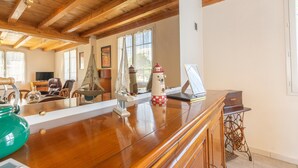 Amplia habitación con vigas de madera, una mesa de madera pulida, un hervidor verde y un modelo de faro rojo y blanco.