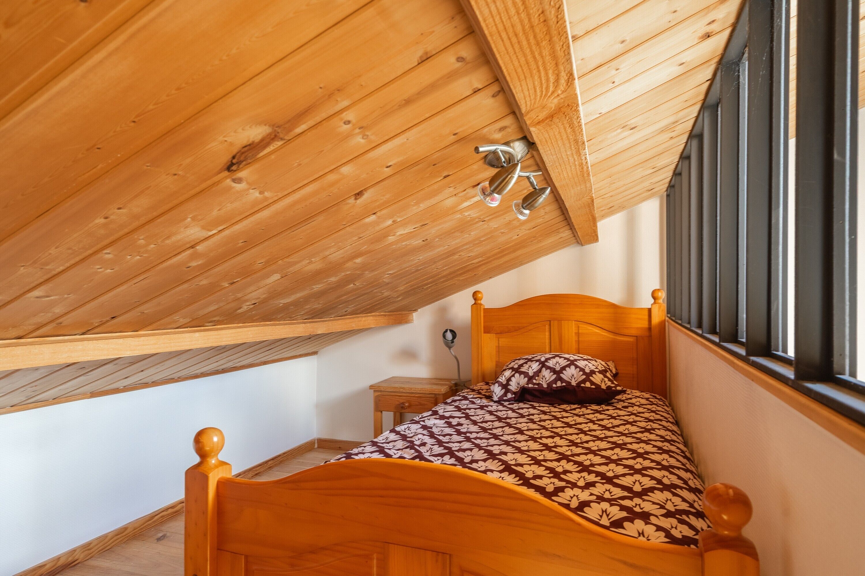 Un plafond en bois avec une fenêtre, un lit recouvert d’une couvre-lit à motifs et une table de chevet.