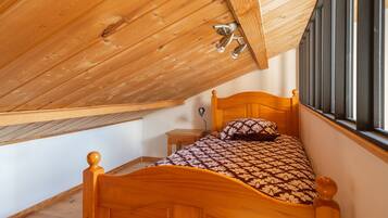 Un plafond en bois avec une fenêtre, un lit recouvert d’une couvre-lit à motifs et une table de chevet.