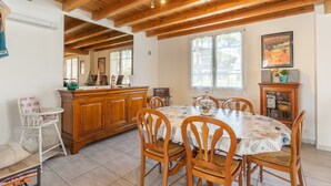 Un comedor con sillas de madera, una mesa con mantel, un armario de madera y una ventana con un cartel.