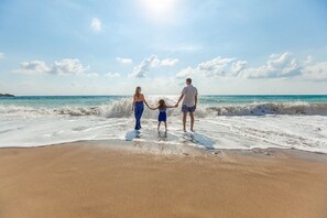 A family holding hands on a sandy beach with waves, under a clear sky. -  Updated Oceanfront 2 br. getaway balcony view, steps to pool, walk to beach! (Hilton Head Island)