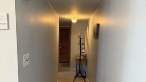 Un pasillo estrecho con piso alfombrado, una puerta de madera al final y un atril con un cuadro enmarcado.