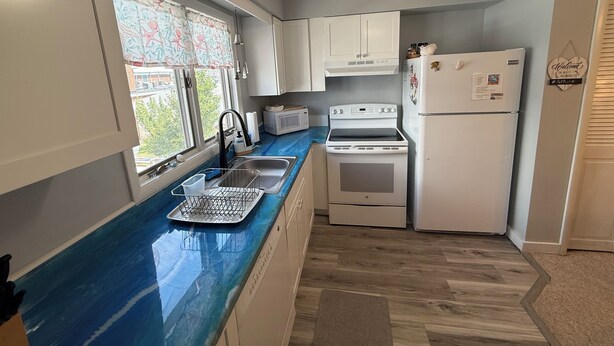 Una cocina con encimera azul, armarios blancos, estufa, refrigerador y ventilador de techo.