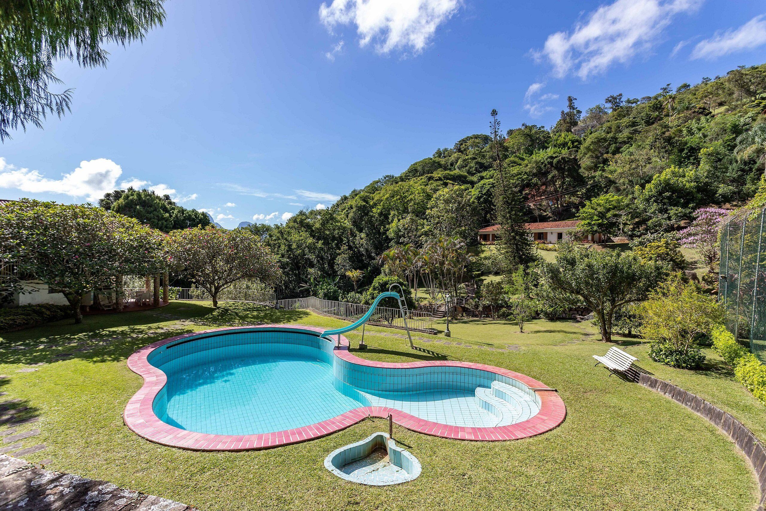 A swimming pool with a slide, surrounded by a grassy area and trees.