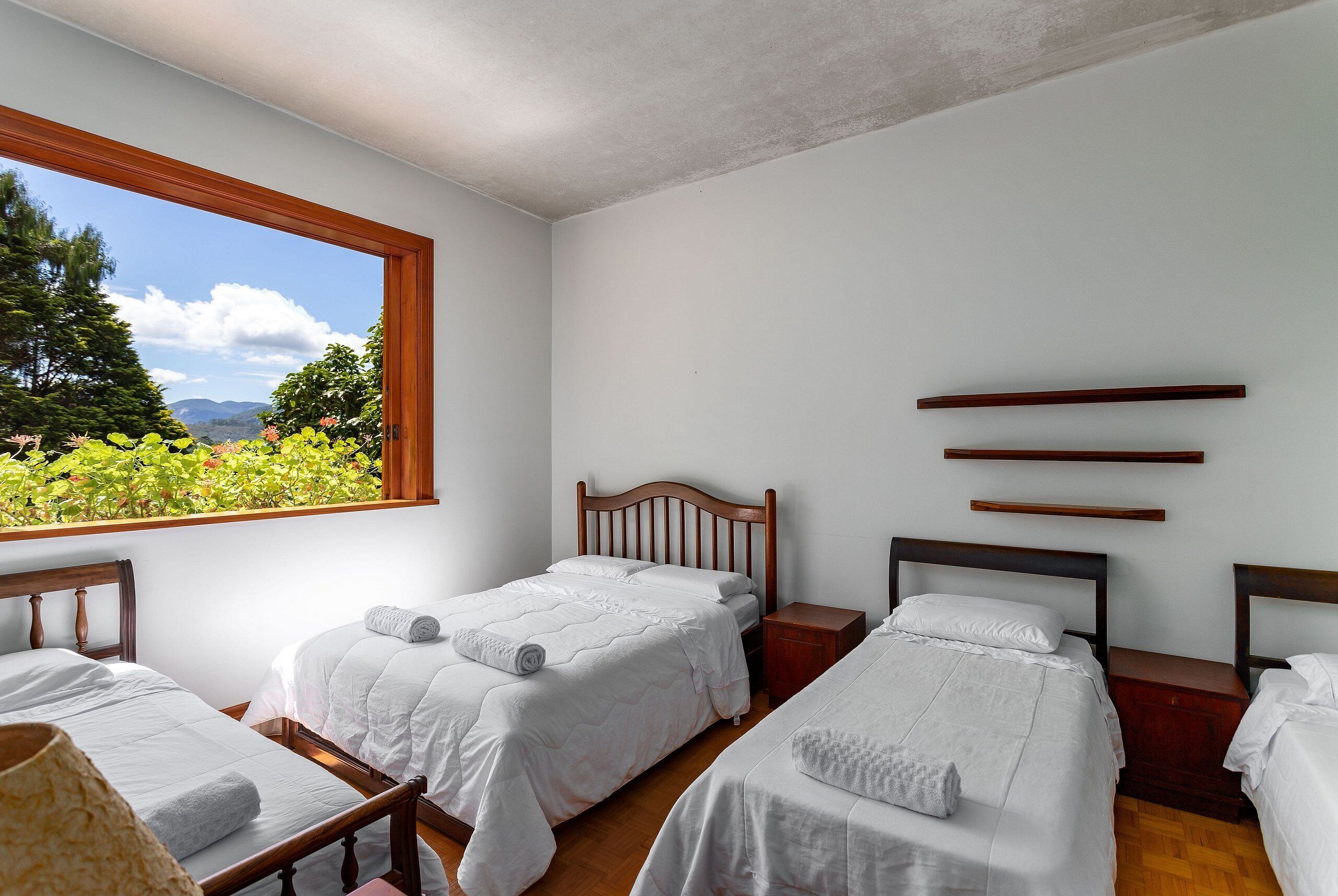 Una habitación con tres camas, cabeceros de madera y un ventanal con vistas a zonas verdes y montañas.