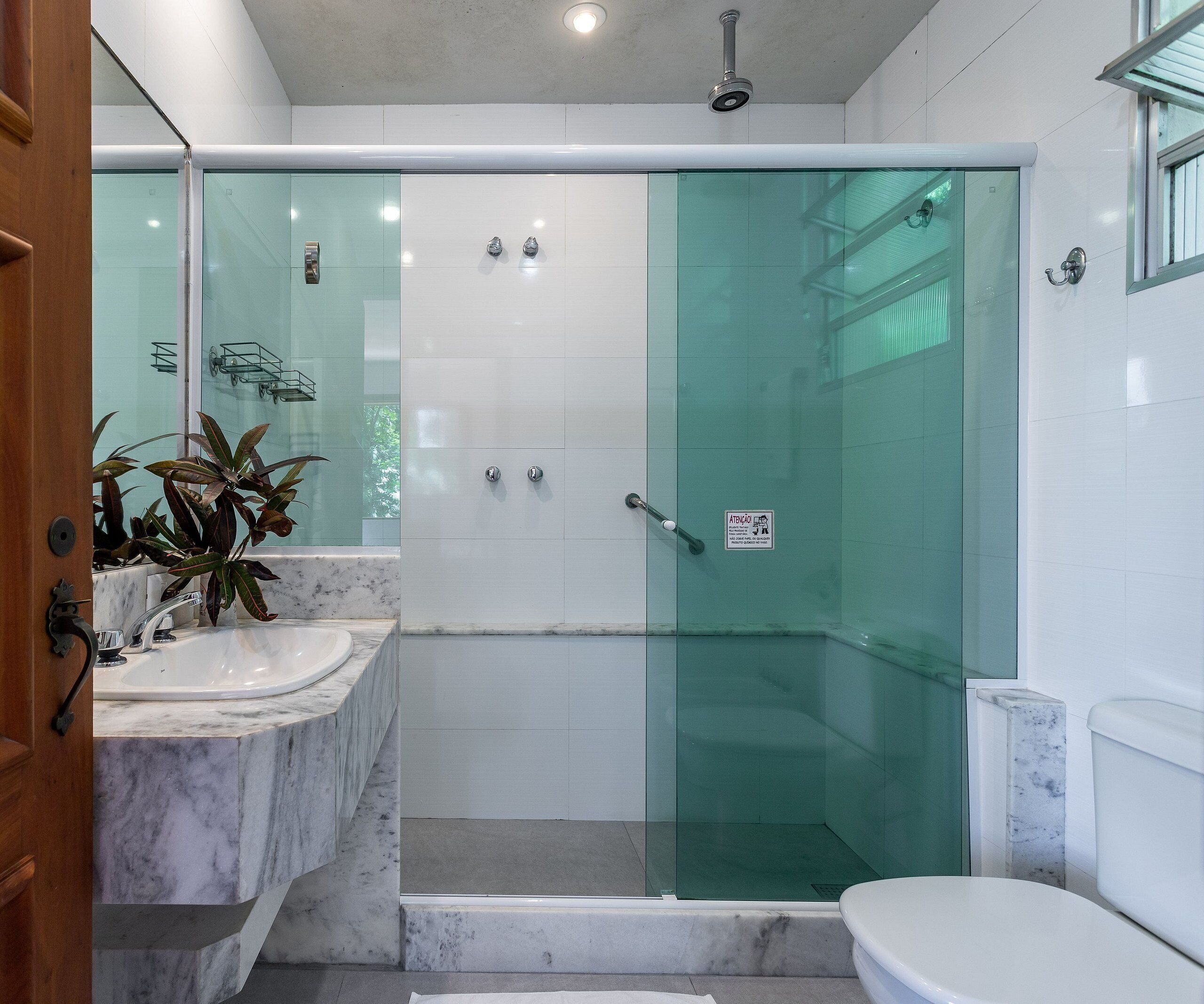 Uma casa de banho moderna com chuveiro envolto em vidro, lavatório de mármore e sanita.