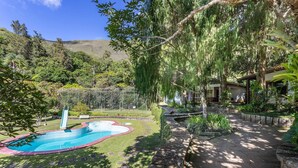 Ein Garten mit Swimmingpool, einer Terrasse und Blick auf eine Hügelkette.