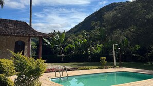 Una piscina con suelo de baldosas, un edificio de piedra con tejado de baldosas y una palmera.