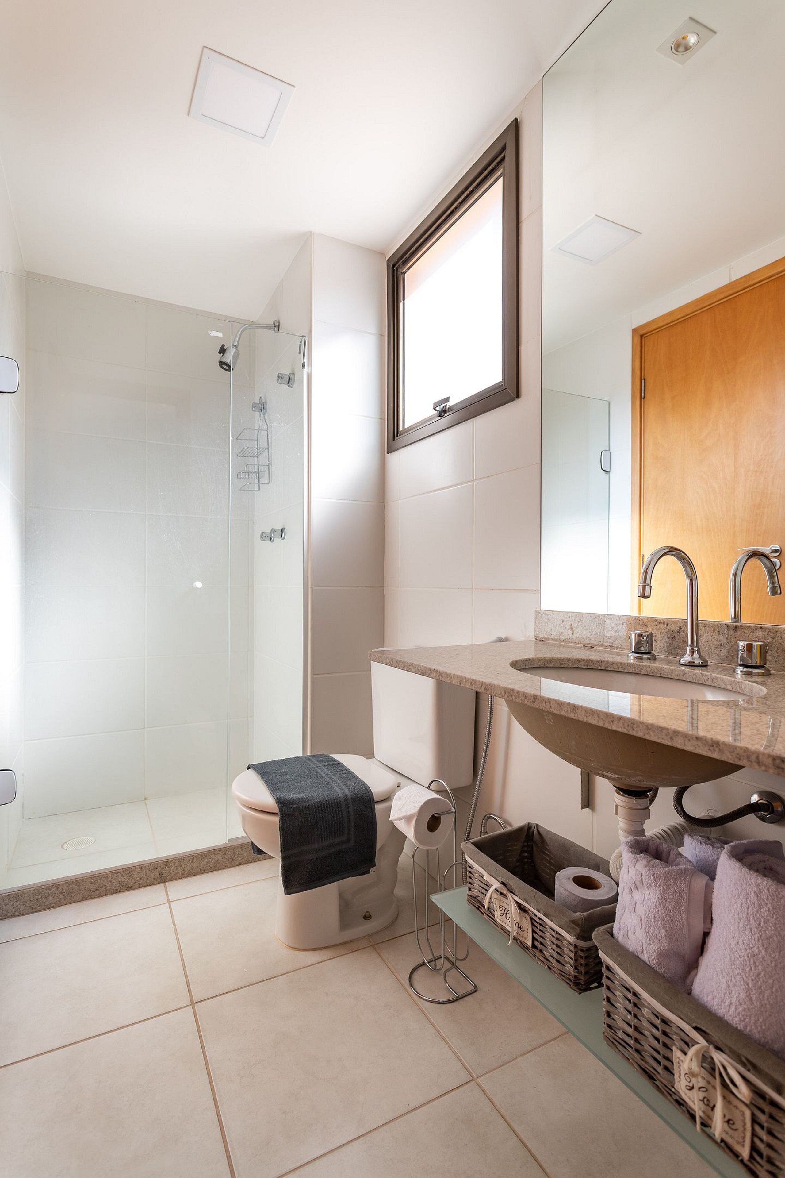 Un baño moderno con ducha acristalada, inodoro con toalla y lavamanos con espejo superior.