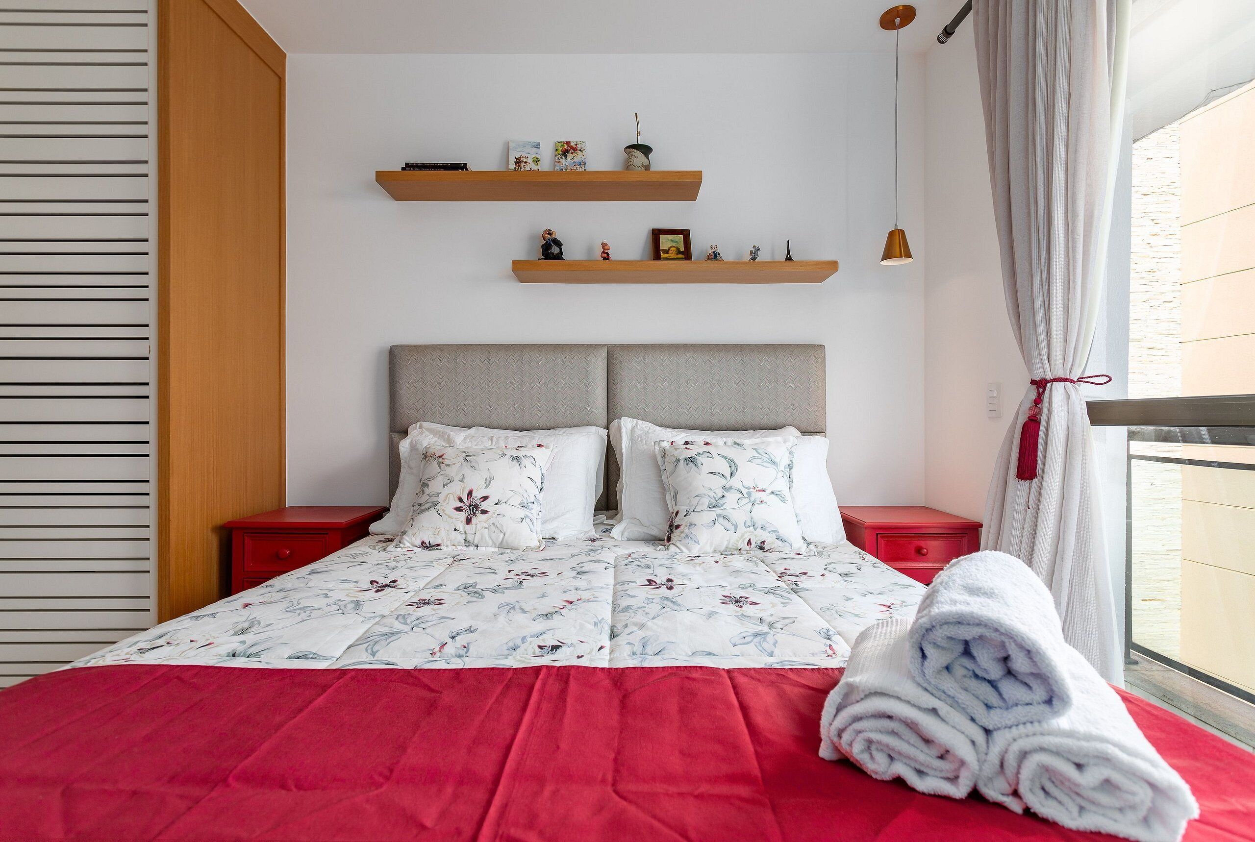 A neatly made bed with floral bedding, two nightstands, and a window with curtains.