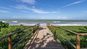 Une promenade en bois menant à une plage où l’on peut voir des vagues, le tout étant entouré de verdure.