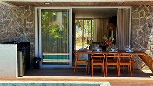 Un espace repas aménagé au bord de la piscine, avec une table dressée pour quatre personnes, entouré de murs en pierre et offrant une vue sur la piscine.