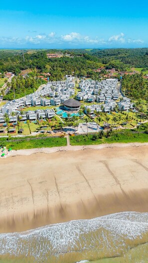 Um resort com vários edifícios, piscina central e acesso à praia.