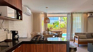 Une cuisine moderne avec un îlot central, un coin repas avec des chaises en osier et une vue sur une piscine.