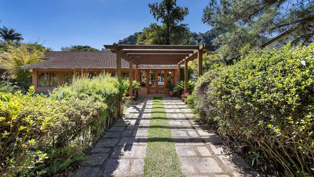 A covered wooden structure with a tiled roof, surrounded by lush greenery and a stone pathway leading to it. - Granja Comary House with private pool and jacuzzi (Teresópolis)