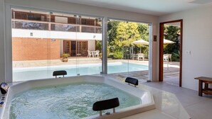 A modern hotel room with a large bathtub, a balcony, and a view of a swimming pool and garden. - Granja Comary House with private pool and jacuzzi (Teresópolis)