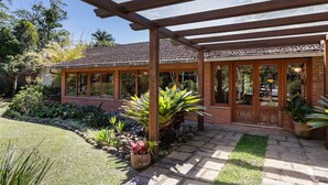 A covered patio area with a pergola, a brick building with large windows, and a well-maintained garden with various plants. - Granja Comary House with private pool and jacuzzi (Teresópolis)