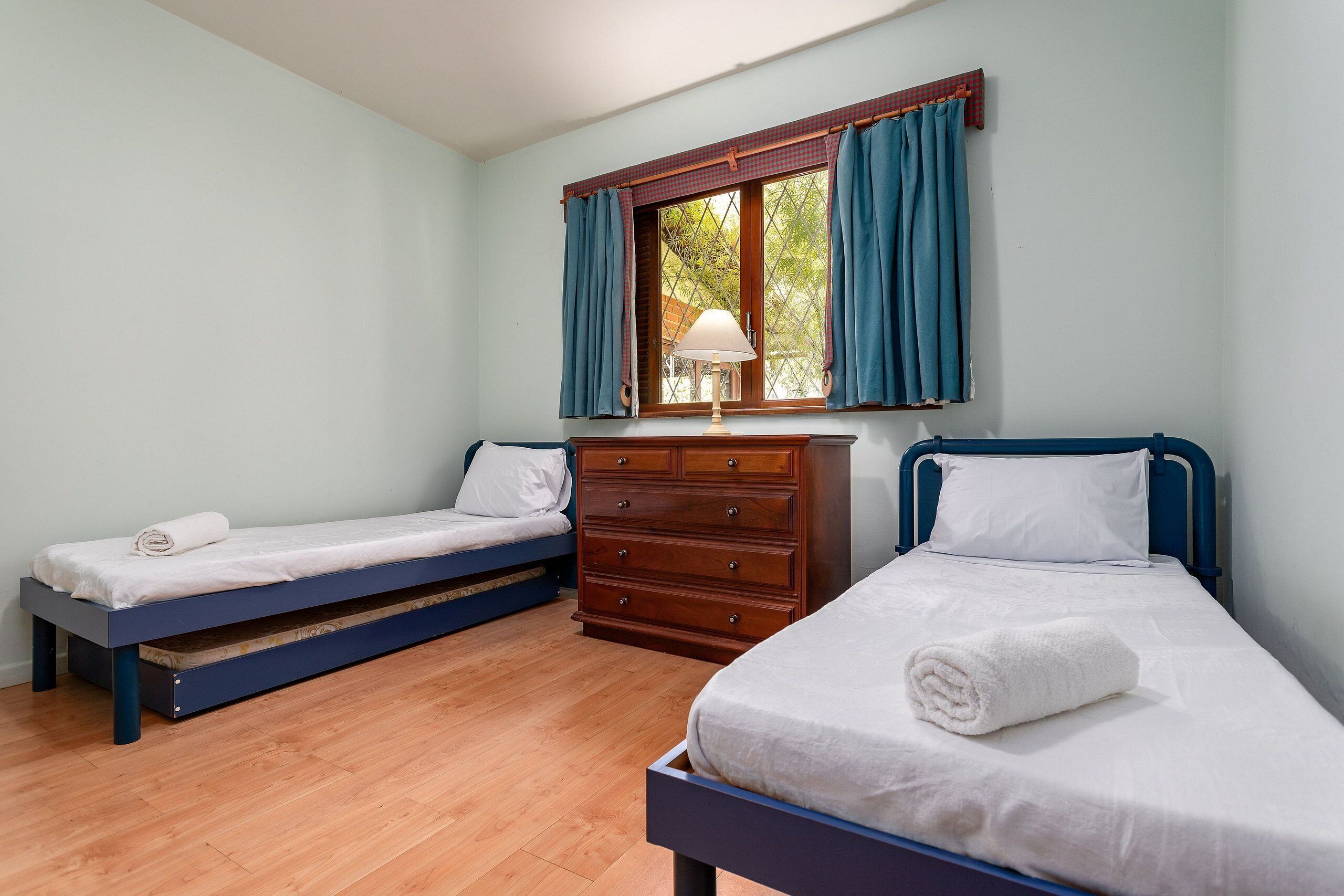 A room with two single beds, a wooden dresser, and a window with curtains.