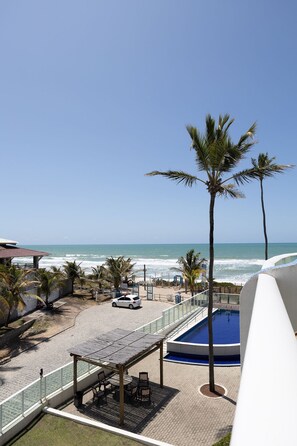 Ein Poolbereich mit Blick auf den Ozean, Palmen und einer überdachten Sitzgelegenheit.