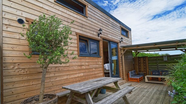 Una cabaña de madera con terraza, mesa de picnic y zona de estar cubierta.