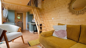 Un interior acogedor de madera con un sofá, una silla, una escalera y una zona de cocina.
