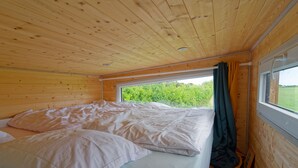 Una habitación de cabaña de madera con una cama, un ventanal y vistas al verdor exterior.
