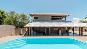 En swimmingpool med en overdækket terrasse, en murstensmur og en klar blå himmel.