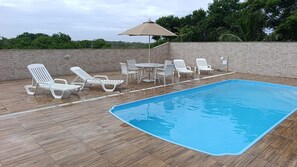 Une piscine entourée d’un mur de briques et de verdure, avec des chaises longues et une table à proximité.