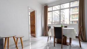 Un coin repas avec une table et des chaises, une fenêtre avec des rideaux et une porte donnant sur une autre pièce.