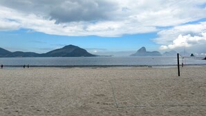 Une plage avec un filet de volley-ball, un sol sablonneux et des montagnes qui se dessinent à l’horizon.