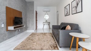 Un salon moderne avec un canapé gris, un téléviseur fixé sur un panneau en bois, un miroir rond et des œuvres d’art abstraites accrochées au mur.