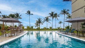 A swimming pool with lounge chairs and umbrellas, surrounded by palm trees and a clear sky. - Flat beach front Itah Residence – Muro Alto/PE (Muro Alto)
