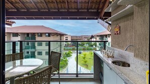 A balcony with a round table and chairs, a sink, and a view of a courtyard with buildings in the background. - Flat beach front Itah Residence – Muro Alto/PE (Muro Alto)