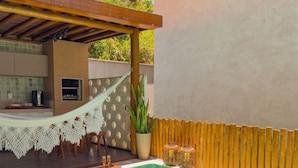 A swimming pool with a tiled deck, a wooden pergola, and a small outdoor kitchen area. - House with Private Pool in Maragogi – Praia de Antunes (Maragogi)