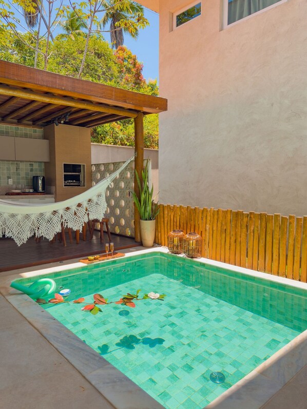 A swimming pool with a tiled deck, a wooden pergola, and a small outdoor kitchen area. - House with Private Pool in Maragogi – Praia de Antunes (Maragogi)