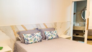 A bedroom with a bed, a nightstand, a bedside table, an air conditioning unit, a bathroom with a mirror, and a towel rack. - Comfort, location, and unforgettable landscapes in Maragogi! (Maragogi)