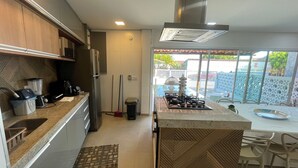 A compact kitchen with a built-in stove, a refrigerator, and a sink. - Comfort, location, and unforgettable landscapes in Maragogi! (Maragogi)