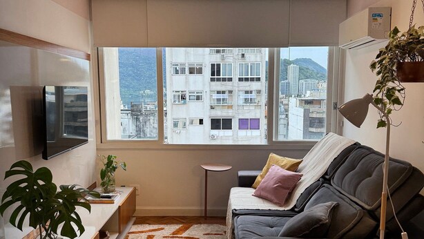 A modern living room with a sofa, a coffee table, a TV, and a large window with a city view.
