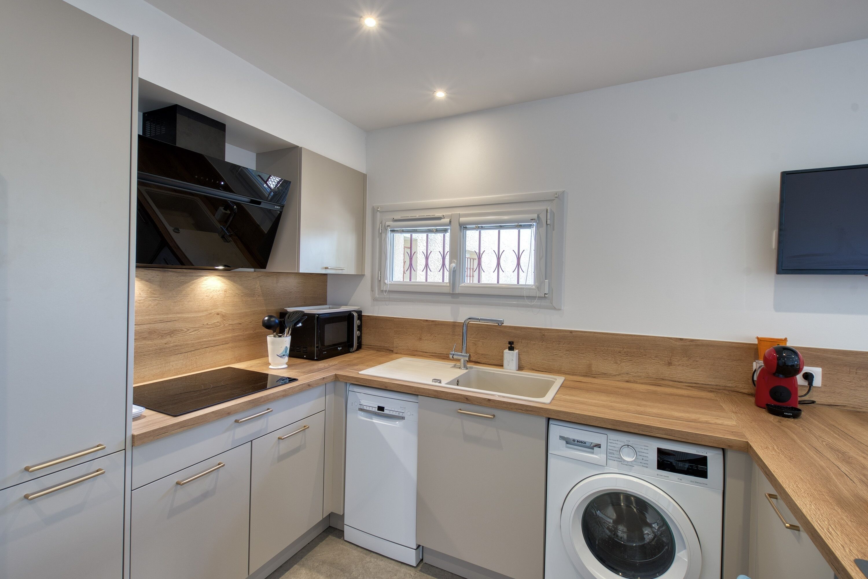 A modern kitchen with a dishwasher, microwave, sink, and a washing machine.
