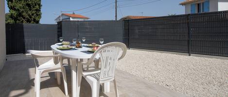 An outdoor patio with a round table and four white chairs, surrounded by a black fence and a gravel area.