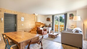 A cozy living room with a wooden dining table, a sofa, and a staircase leading to an upper level.