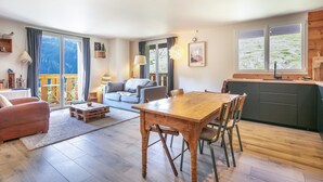 A spacious living area with a wooden dining table, a sofa, and a kitchen with a large window.