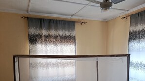 A single bed with a mosquito net, a ceiling fan, and patterned floor tiles. - DZOMBO VIEW GARDENS HOTEL MENZAMWENYE (Vitsangalaweni)