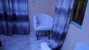 A room with a white armchair, a white chair, and a window with a view. - DZOMBO VIEW GARDENS HOTEL MENZAMWENYE (Vitsangalaweni)