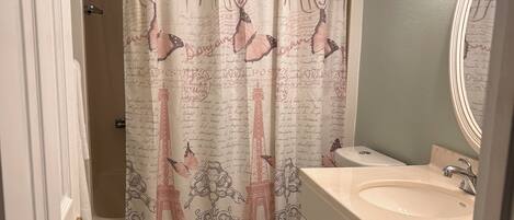 Un baño con cortina de ducha con motivos parisinos, un inodoro y un lavabo con espejo.