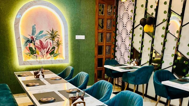 A dining area with a long table, teal chairs, and a green accent wall. - HOTEL D C GRAND (Varanasi)